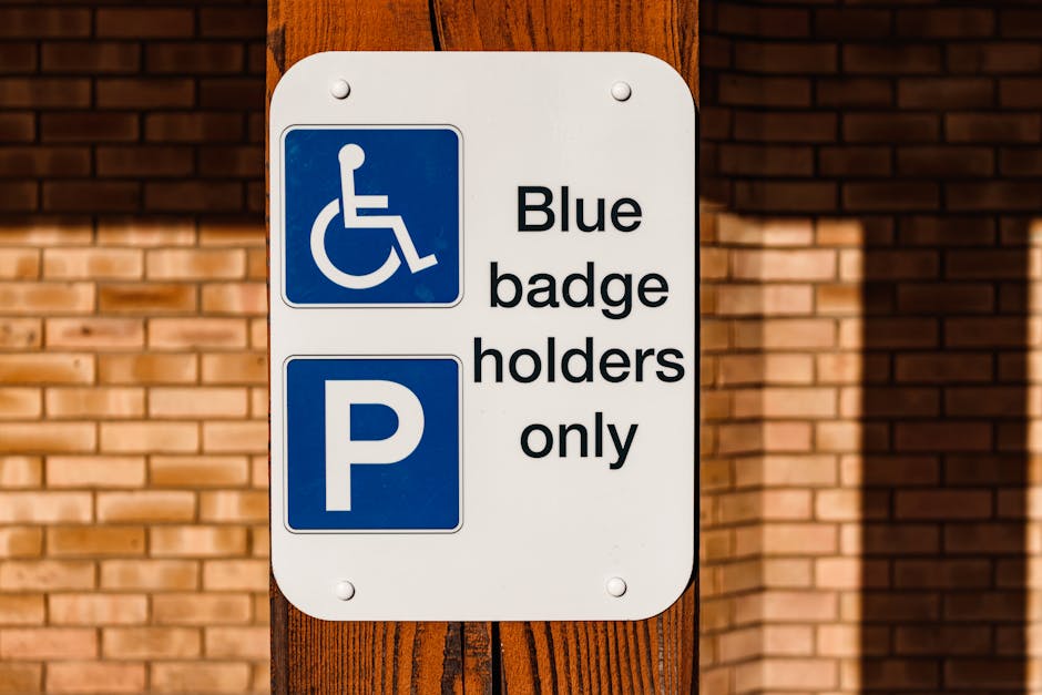 A rectangular white sign attached to a wooden post displays a blue icon of a person in a wheelchair and a large blue 'P' symbol. Next to the icons, black text reads 'Blue badge holders only,' indicating designated parking restrictions. The sign is positioned outdoors against a background of a brick wall, with natural lighting casting subtle shadows on the surface. This signage relates to parking regulations that may be relevant during house removals or furniture transport, as part of the logistical planning by Removal Companies Pimlico for safe and compliant loading areas in PIMLICO.
