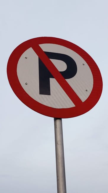 A circular traffic sign with a white background, a bold black letter 'P', and a red circle with a diagonal line through it, indicating no parking. The sign is mounted on a metal pole situated outdoors under an overcast sky. The background shows a plain, light grey sky with no additional objects or structures visible. This sign is relevant for road management during house removals and relocation services, such as those provided by Removal Companies Pimlico, especially when planning furniture transport, loading processes, and the staging area for moving trucks.